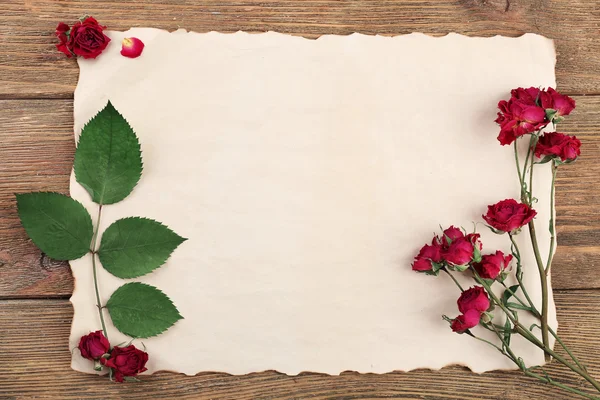 Gedroogde rozen op vel papier op houten tafel, bovenaanzicht — Stockfoto