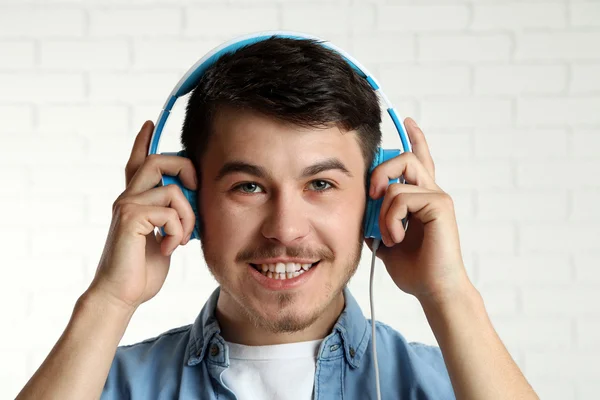 Pohledný mladý muž poslouchat hudbu na pozadí pozadí cihlová zeď — Stock fotografie