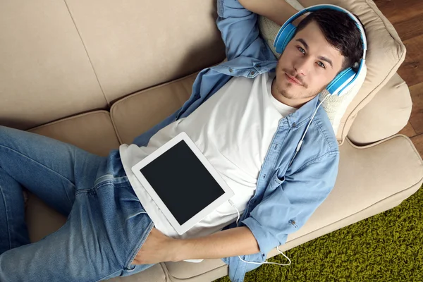 Красивый молодой человек лежит на диване и слушает музыку в комнате — стоковое фото
