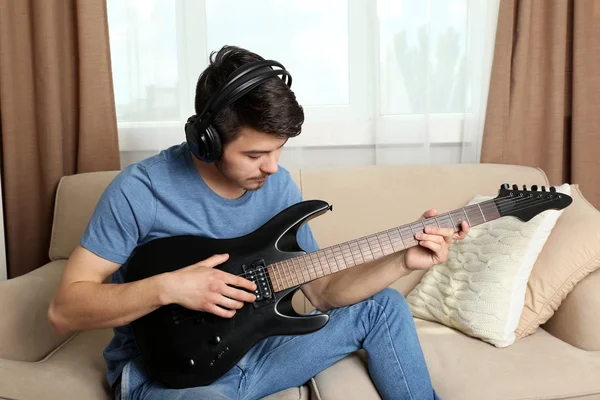 Joven con la guitarra en el sofá en la habitación —  Fotos de Stock