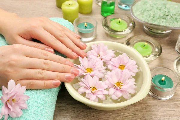 Mãos femininas e tigela de água termal com flores, close-up — Fotografia de Stock