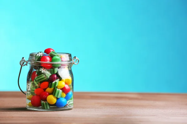 Coloridos caramelos en frasco sobre la mesa sobre fondo azul —  Fotos de Stock