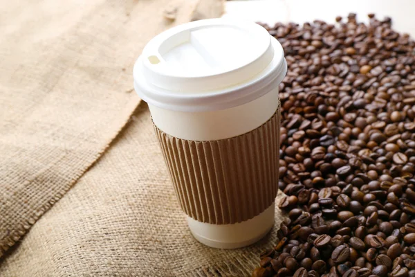 Papieren kopje koffie met bonen op zak close-up — Stockfoto