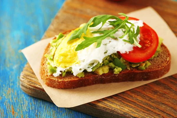 Tasty sandwich with egg, avocado and vegetables on cutting board, on color wooden background — Stock Photo, Image