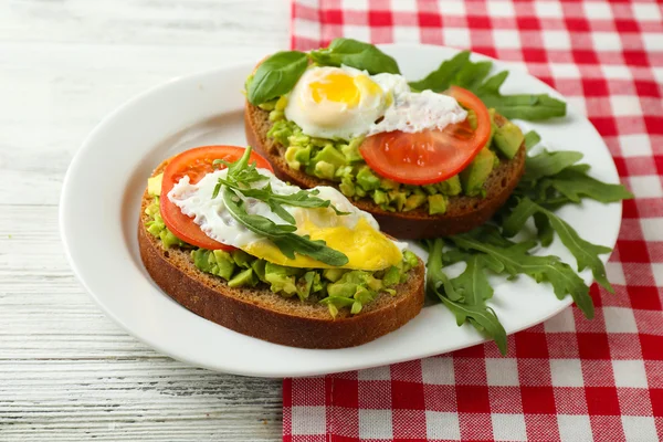 Läckra mackor med ägg, avokado och grönsaker på tallriken, på trä bakgrund — Stockfoto