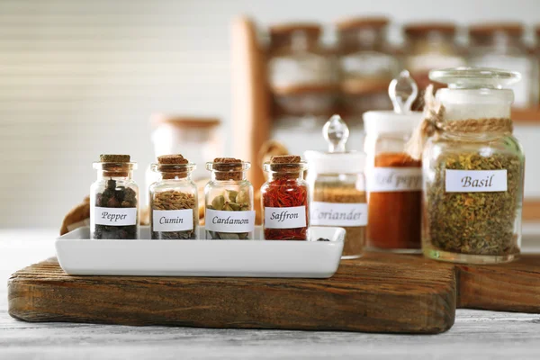 Assortimento di spezie in bottiglie di vetro su tagliere, su fondo di legno — Foto Stock