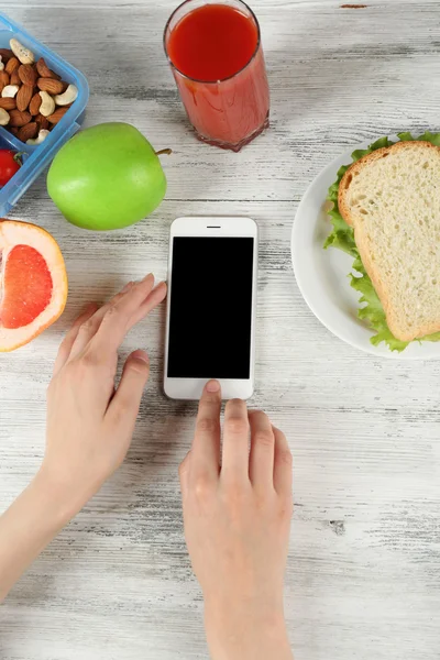 Еда и мобильный телефон в женских руках на деревянном фоне — стоковое фото