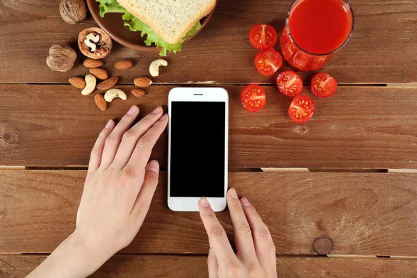 Їжа та мобільний телефон у жіночих руках на дерев'яному фоні — стокове фото