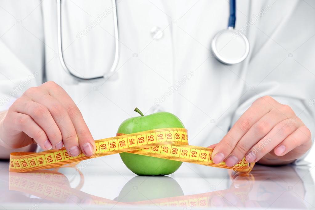 Nutritionist doctor with apple and measuring tape, closeup