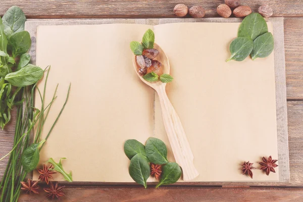 Livre de recettes ouvert avec cuillère et herbes sur fond en bois — Photo