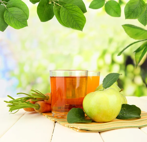 Glazen van SAP, appelen en wortelen op tafel, buitenshuis — Stockfoto