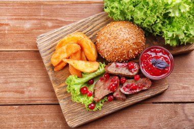 Kızılcık sosu, kavrulmuş patates dilimleri ve ahşap arka plan üzerinde kesme tahtası üzerinde topuz ile sığır eti