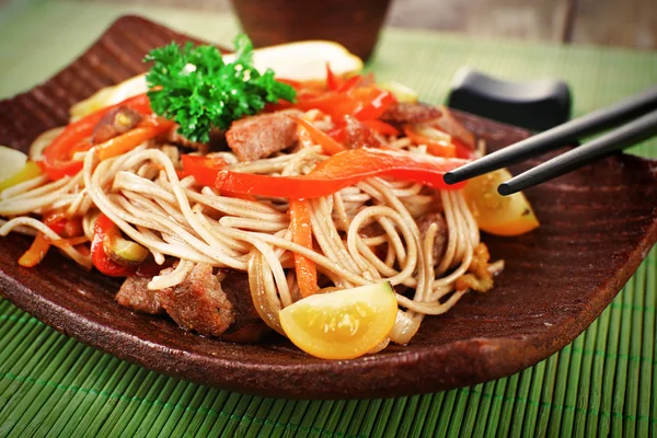 Macarrão chinês com legumes e carne assada no fundo da esteira de bambu — Fotografia de Stock