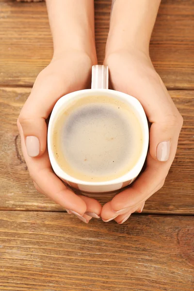 Mãos femininas segurando xícara de café no fundo de madeira — Fotografia de Stock