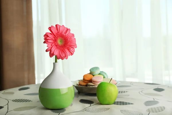 Color gerbera flor en jarrón y manzana con macarrones en la mesa sobre el fondo de cortinas —  Fotos de Stock