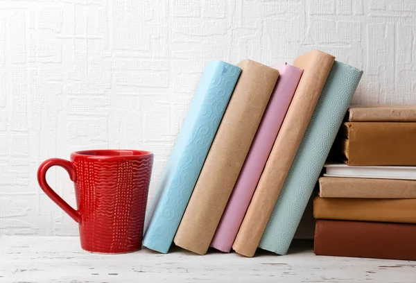 Books and cup on wooden shelf on wallpaper background