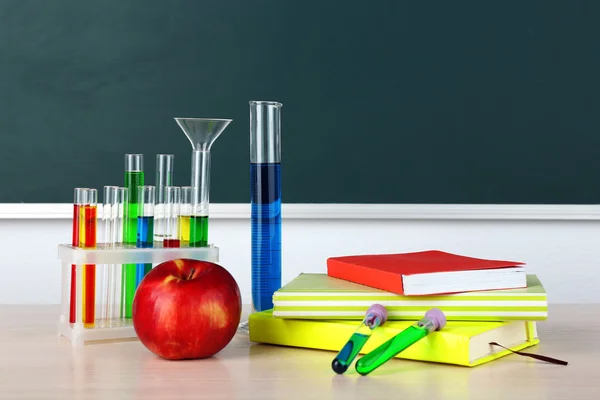 Desk in chemistry class with test tubes on green blackboard background