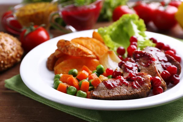 Wołowina z sosem żurawinowym, ziemniaki pieczone plastry, warzyw na talerzu, na tle drewniane — Zdjęcie stockowe
