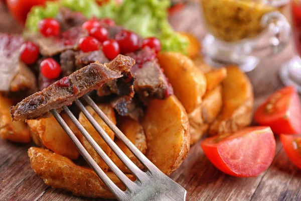 Beef with cranberry sauce, roasted potato slices and bun on cutting board, on wooden background