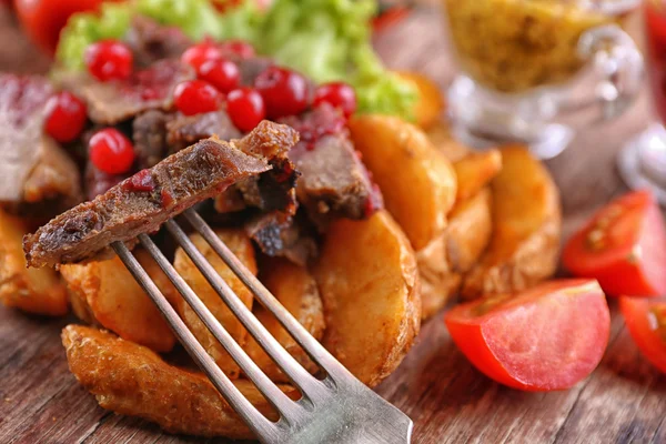 Beef with cranberry sauce, roasted potato slices and bun on cutting board, on wooden background — Stock Photo, Image