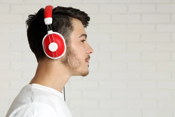 Pohledný mladý muž poslouchat hudbu na pozadí pozadí cihlová zeď — Stock fotografie