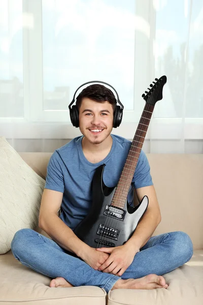 Joven con la guitarra en el sofá en la habitación —  Fotos de Stock