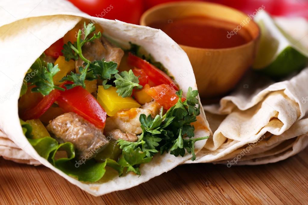 Homemade tasty burrito with vegetables, potato chips on cutting board, on wooden background
