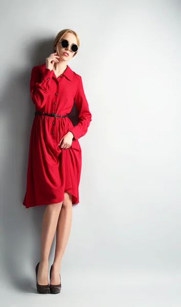Ekspresyjny młody model w czerwonej sukience i okulary na szarym tle — Zdjęcie stockowe