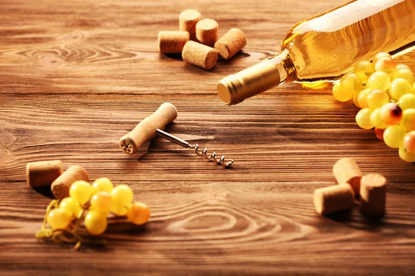 Glass bottle of wine with corks, corkscrew and grapes on wooden table background — Stock Photo, Image