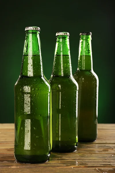 Glazen flessen bier op donkere groene achtergrond — Stockfoto