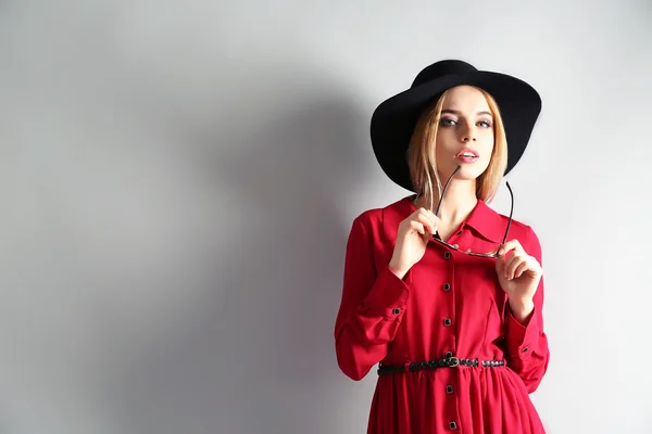 Modelo joven expresivo en vestido rojo y sombrero negro sobre fondo gris —  Fotos de Stock