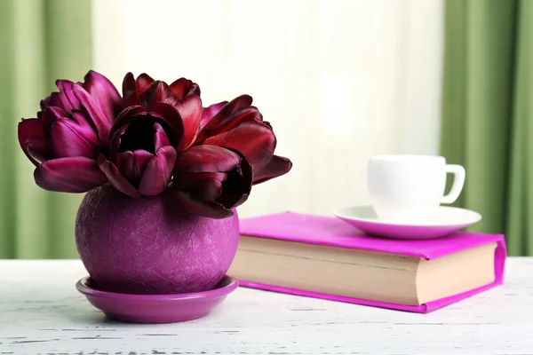 Красивые тюльпаны в горшочке с книгой на фоне ткани — стоковое фото