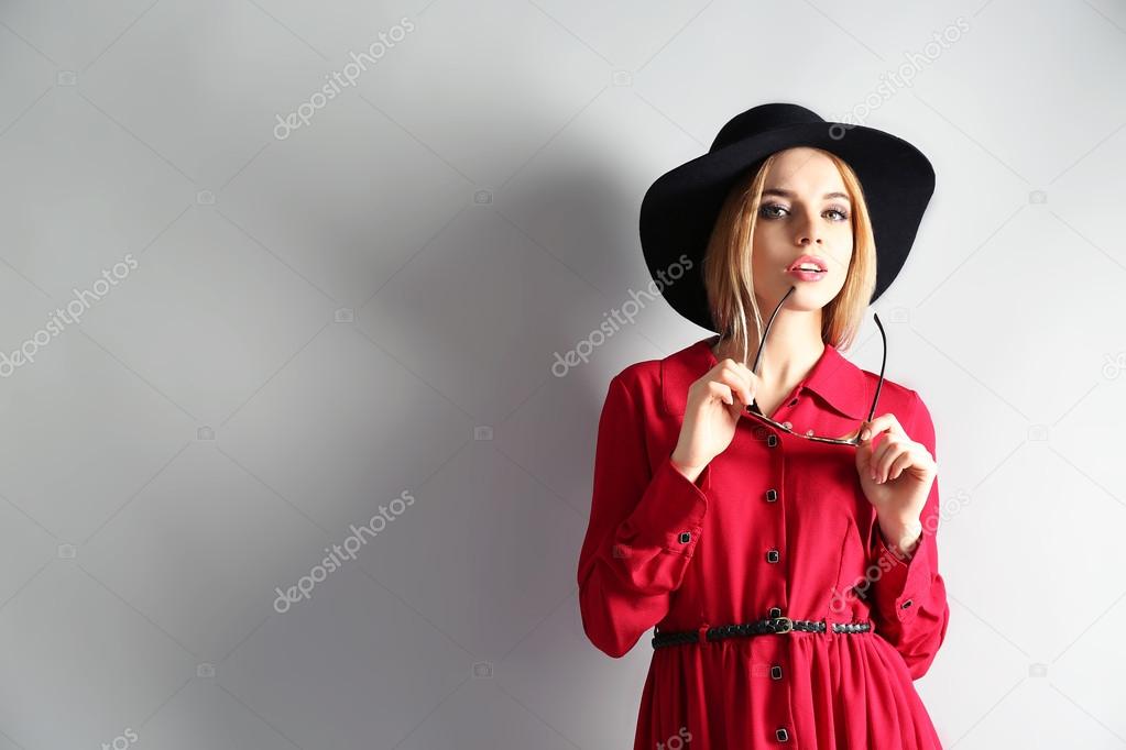 Expressive young model in red dress and black hat on gray background