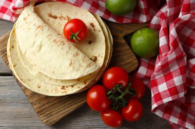 Ev yapımı kepekli un tortilla ve ahşap masa arka plan üzerinde kesme tahtası üzerinde sebze yığını