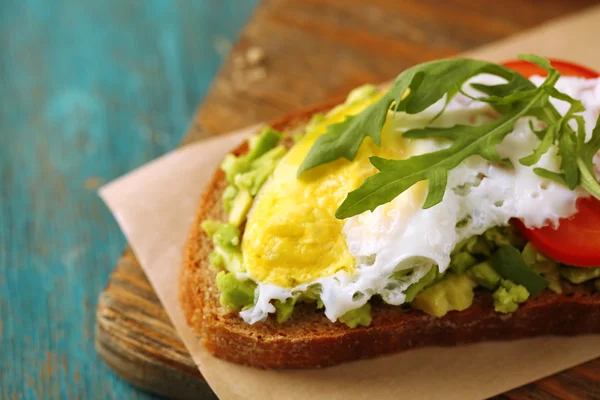 Tasty sandwich with egg, avocado and vegetables on cutting board, on color wooden background — Stock Photo, Image