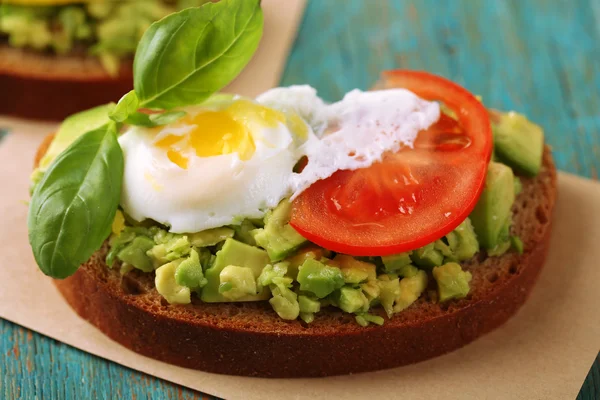 Sanduíche saboroso com ovo, abacate e legumes em guardanapo de papel, na cor de fundo de madeira — Fotografia de Stock