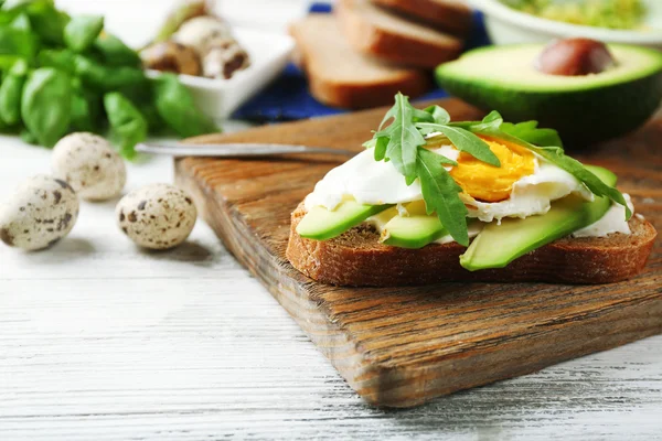 Tasty sandwich with egg, avocado and arugula on wooden background