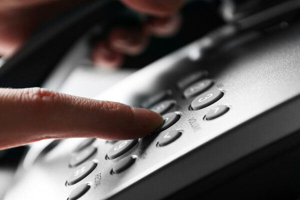 Finger pressing number button on telephone to make a call, close up