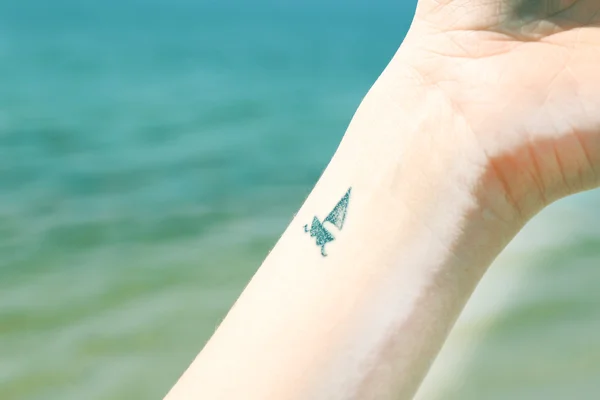 Κοντινό πλάνο του καρπού νεαρής γυναίκας με πλοίο τατουάζ σε αυτό, στο θαλασσινό background — Φωτογραφία Αρχείου