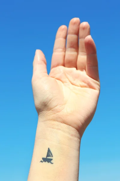 Close up of hand of young woman with ship tattooed in it, sky background — Stock Photo, Image