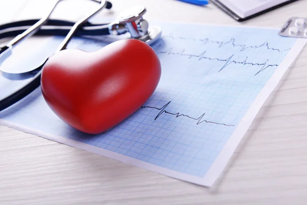 Cardiograma com estetoscópio e coração vermelho na mesa, close-up — Fotografia de Stock