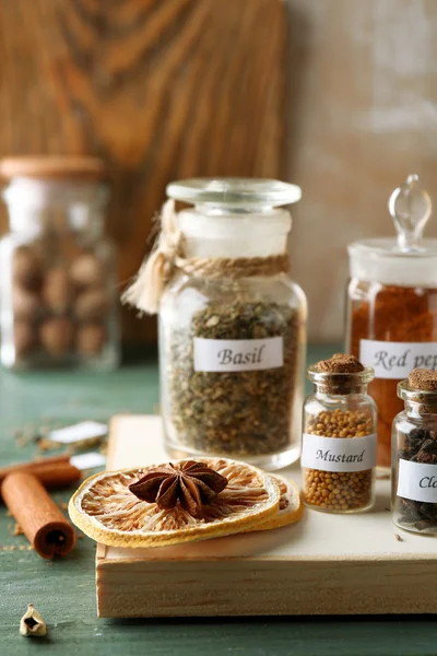 Assortiment van specerijen in glazen flessen op snijplank, op houten achtergrond — Stockfoto