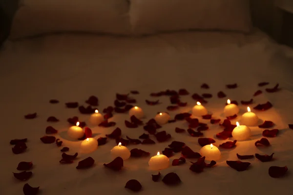 Heart of candles and red petals on bed, close up — Stock Photo, Image