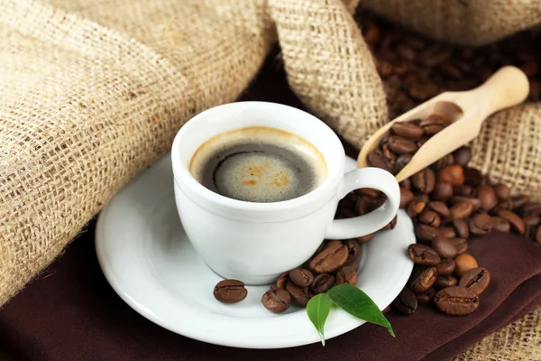 Tasse Kaffee mit Bohnen auf dem Tisch aus nächster Nähe — Stockfoto