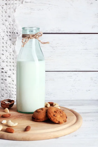 Lait en verrerie avec noix et biscuits sur fond bois — Photo