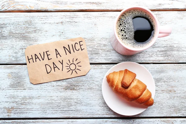 Kopp kaffe med färsk croissant och Have A Nice Day massage på träbord, ovanifrån — Stockfoto