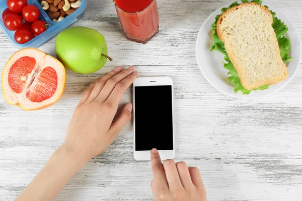 Gıda ve ahşap arka plan üzerinde eller içinde hareket eden telefon