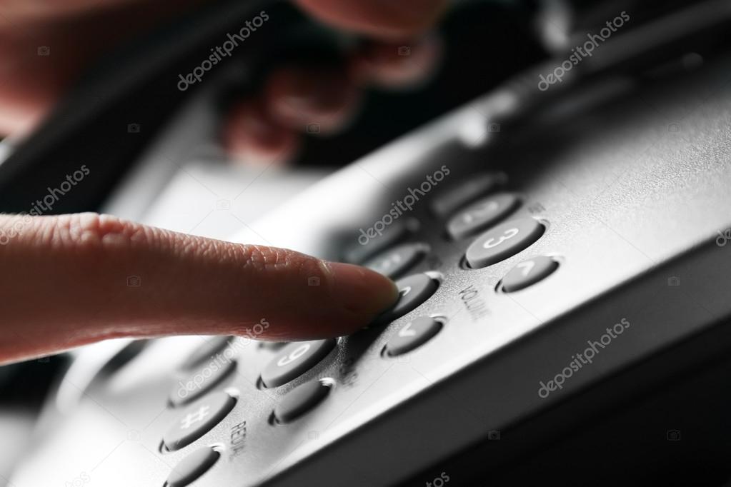 Finger pressing number button on telephone to make a call, close up