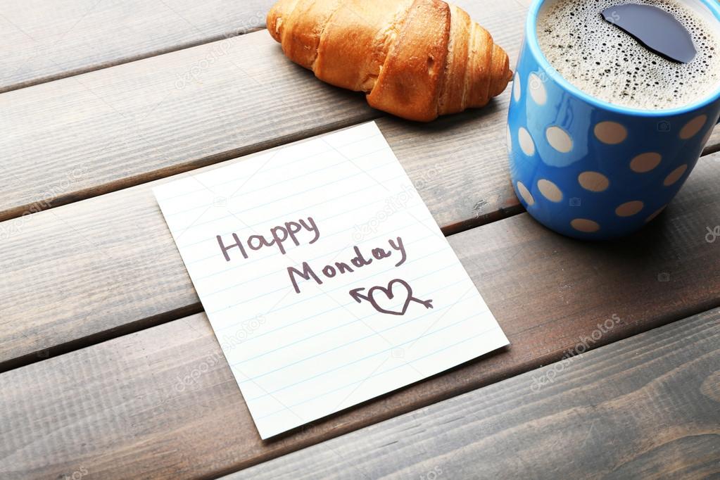 Cup of coffee with fresh croissant and Happy Monday massage on wooden background
