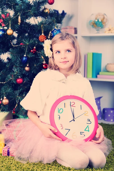 Chica sosteniendo reloj cerca de árbol de Navidad — Foto de Stock